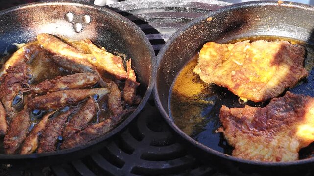Outdoor cooking small fried fish and fish fillets in hot oil on cast iron pans