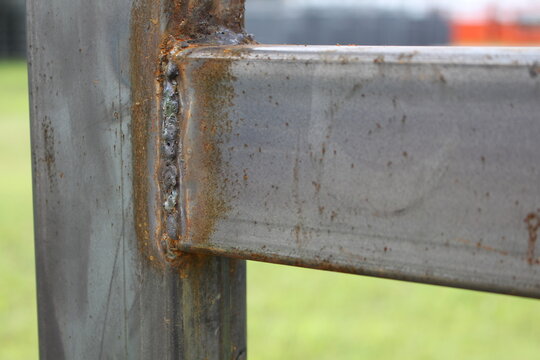 Close-up of a rusty weld joining square steel tubes on a fence