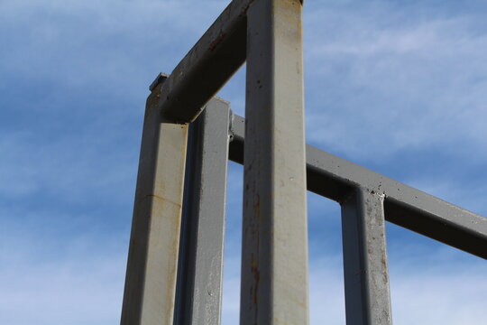 Corner of a gray steel livestock pen frame against a blue sky
