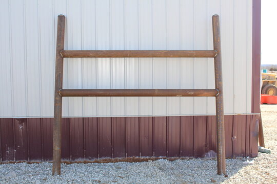 Rusty steel pipe H frame leaning against a metal building wall