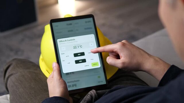 Facility worker monitors building zones and adjusts office climate settings on a tablet, highlighting smart HVAC control, energy efficiency and connected workplace management.