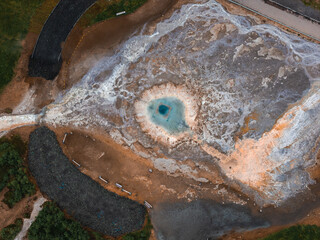 Aerial top down perspective shows the boiling thermal pool of Strokkur geyser surrounded by mineral deposits, hiking paths, and geothermal ground in Haukadalur valley, Iceland. © Aerial Film Studio