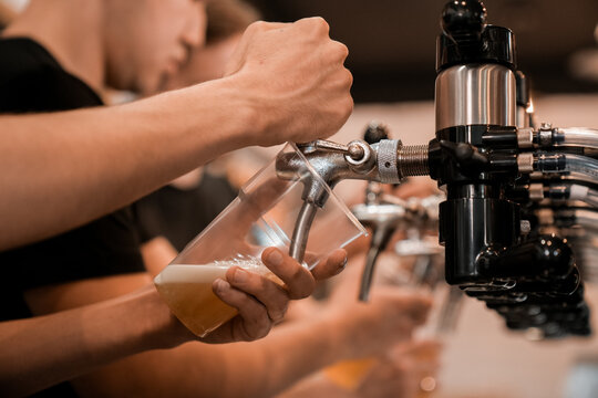 Close-up of a bartender pouring draft beer from a tap into a glass at a bar.