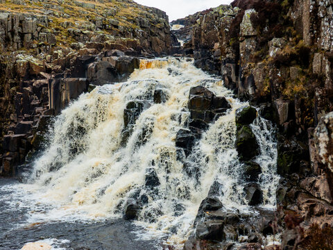 View of Cauldron Snout waterfall cascading over dark basalt rocks in the rugged landscape of the North Pennines, with rushing water in Barnard Castle, England, United Kingdom.