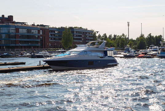 Luxury yacht glides across shimmering waterway. Sunlight dances on gentle ripples, reflecting off calm surface. Modern buildings line distant shore, adding urban contrast