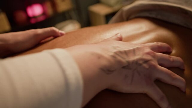 Caucasian massage therapist kneading oiled back of African American woman during therapy session. Footage suited for spa marketing, physical rehabilitation, and wellness campaigns