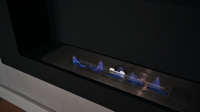 Modern linear gas burner with blue flames, metallic surface, minimalist design, sleek control knobs, dark surround