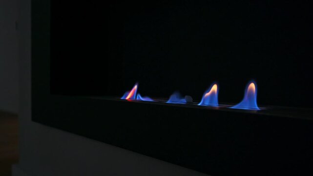 Modern linear gas burner with blue flames, metallic surface, minimalist design, sleek control knobs, dark surround