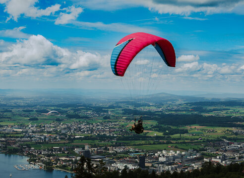 View of a paraglider soaring above the town of Zug, with the lake, green fields, and distant mountains under a blue sky with white clouds Zug, Zug, Switzerland.