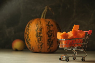 Tiny shopping cart carries bright squash beside a striped pumpkin © Nazar 