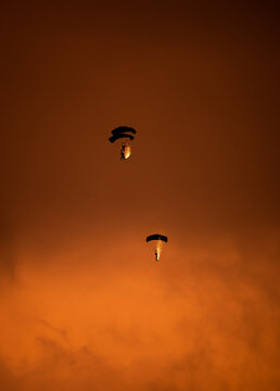 View of two skydivers descending with pyrotechnics trailing sparks against a vibrant orange sunset sky, Otopeni, Judetul Ilfov, Romania.
