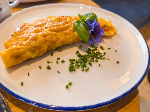 Toblach, Italy. Golden Omelette with Fresh Basil, Chives and Edible Blue Flower on a White Plate