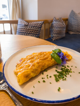 Toblach, Italy. Golden Omelette with Fresh Herbs and Edible Flower in a Cozy Caf&eacute; Setting