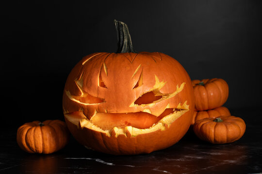 Close-up of a hollowed-out pumpkin with a face carved into it. The background is dark.