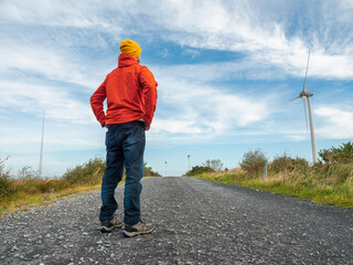 Person stands with arms wide open on gravel road. Red jacket and yellow hat contrast with blue sky. Feels freedom, peace, or adventure. Great for travel, wellness, or outdoor lifestyle themes. © mark_gusev