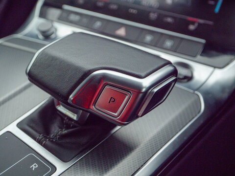 Close-up of modern car's gear shift lever with 'P' parking position illuminated red. Smooth black leather and metallic accents highlight luxury interior. Sleek design suggests high-end vehicle