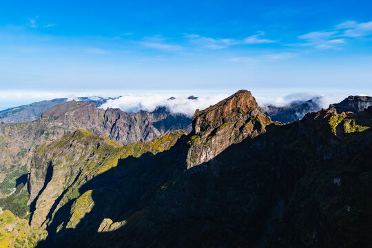 Pico do Arieiro mountain landscape with sunlit ridge and clouds, Madeira, Portugal. Broad mountain scenery with steep cliffs and clear blue sky