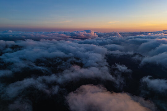 Layered clouds over dark mountain terrain beneath pink dawn sky. Transition from night to morning.