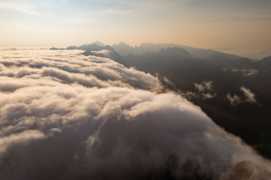 Encroaching cloud cover flowing down mountain slopes and engulfing valley below. Aerial landscape with exposed peaks above cascading clouds