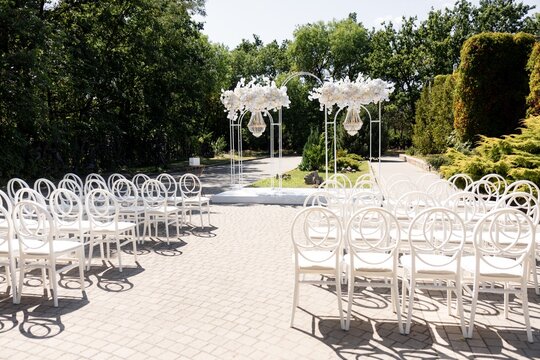 Outdoor wedding ceremony site with white arch and chiavari ghost chairs