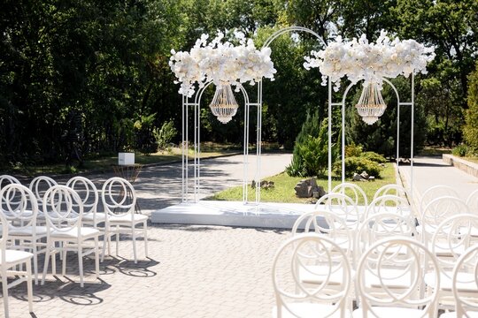 Outdoor wedding ceremony site with white arch and chiavari ghost chairs