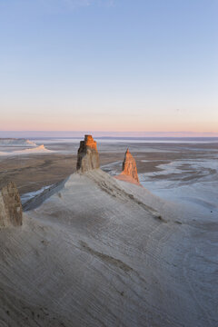 Aerial view of the Lower Fangs rock formations in the Bozhira tract, featuring dramatic limestone cliffs, desert landscape, and soft sunset light in Karakiya District, Mangystau, Kazakhstan.