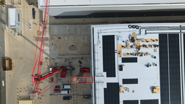 Aerial view of industrial warehouse construction site featuring a red crane, heavy machinery, and solar panel installation on the roof in Daventry, England, United Kingdom.