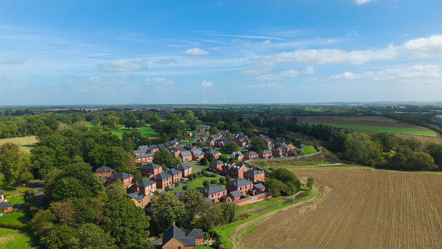 Aerial view of Coton Housing Estate featuring red brick houses surrounded by lush green trees and agricultural fields in Rugby, England, United Kingdom.