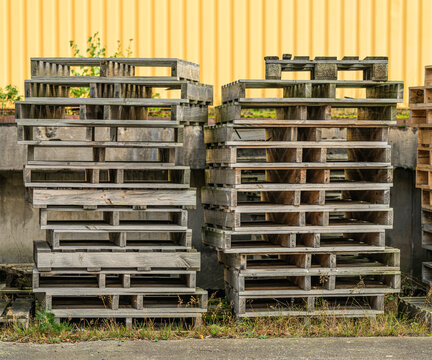 Stacks of weathered wooden shipping pallets outside industrial building.