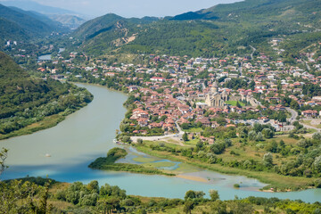 Panoramic view of Mtskheta in Georgia with Svetitskhoveli Cathedral, river confluence, red-roofed houses, wooded hills, and distant mountains © Mila