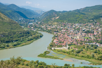 Panoramic view of Mtskheta in Georgia at the confluence of the Kura and Aragvi rivers, with Svetitskhoveli Cathedral, homes, and forested mountains © Mila
