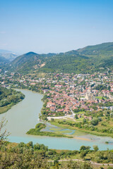 Panoramic view of Mtskheta, Georgia, with the Kura and Aragvi rivers, Svetitskhoveli Cathedral, red rooftops, green hills, and blue sky © Mila