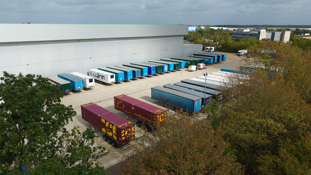 Aerial view of a logistics distribution center with numerous parked HGV trailers arranged in rows next to a large warehouse building in Magna Park, England, United Kingdom.