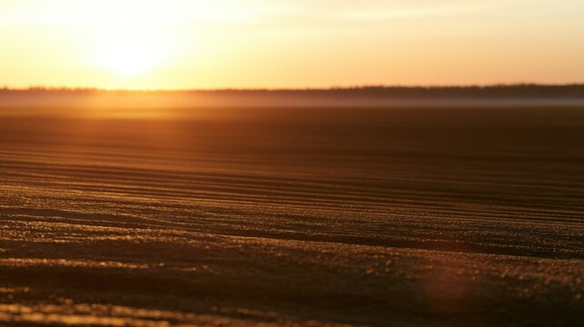 Sun sets beyond a wide field of furrows as the last light reaches the soil