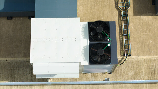 Aerial view of industrial ventilation cooling fans mounted on a flat rooftop with metal ducting and cable trays in Lutterworth, England, United Kingdom.