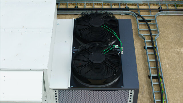 Aerial view of industrial ventilation cooling fans mounted on a rooftop with metal cable trays and concrete surface in Lutterworth, England, United Kingdom.