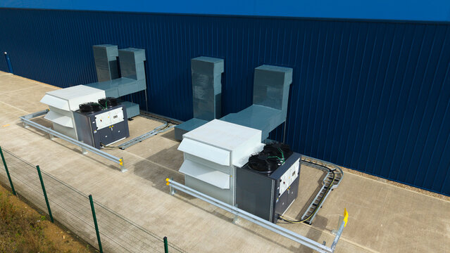 Aerial view of industrial ventilation cooling fans installed on a concrete surface next to a blue metal wall with metal ducting and safety railings in Lutterworth, England, United Kingdom.