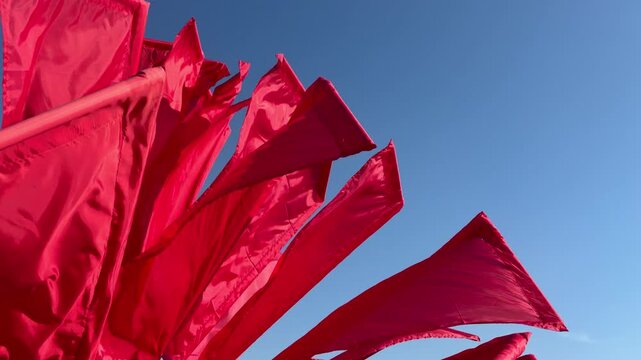 Red flags fluttering in the wind against a clear blue sky. Concepts of politics, protests, , celebrations