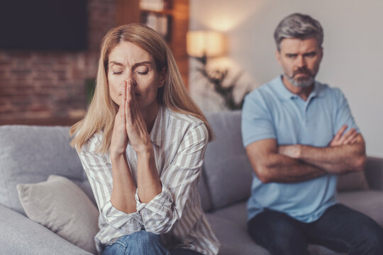 Worried Expression On Face Of Middle-aged Caucasian Woman With Upset Man Sitting On Couch, Engaging In Argumentative Discussion In Modern Living Room, Emotional Distress Concept.