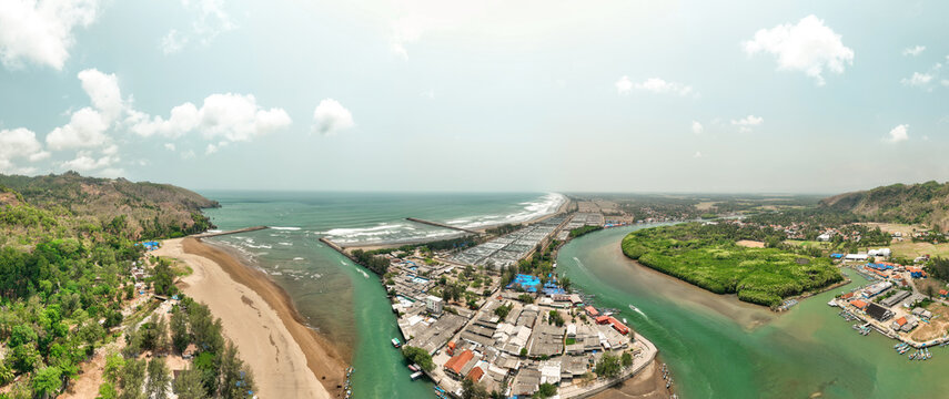 Aerial view of the Cilacap Shrimp Farm located along the river estuary, featuring aquaculture ponds, a sandy beach, lush green mangroves, and small boats in Nusawungu, Central Java, Indonesia.
