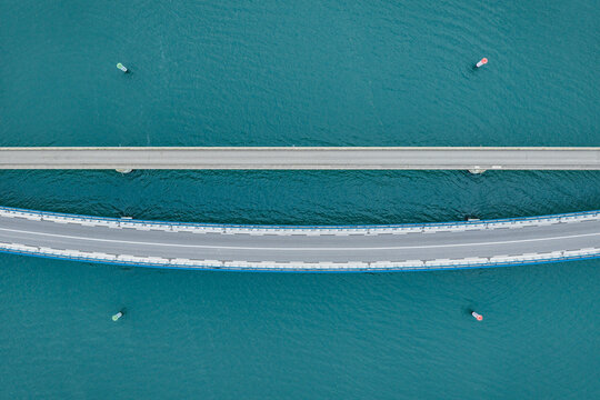 Aerial view of two parallel road bridges, one straight and one curved, crossing turquoise water in Portes-les-Valence, Auvergne-Rhone-Alpes, France.