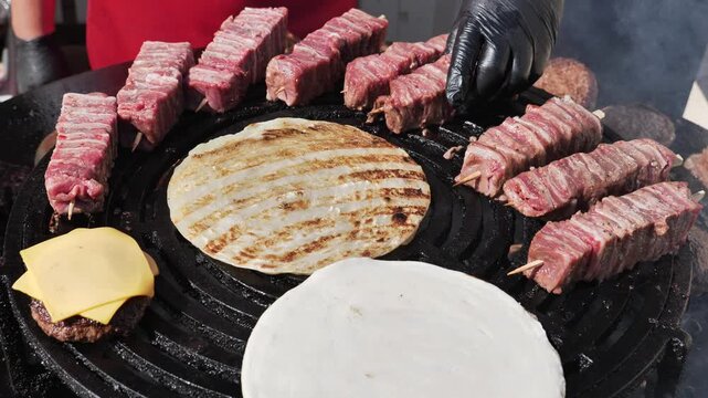 Grilling arrosticini, hamburgers, and pita bread on a large round barbecue grill