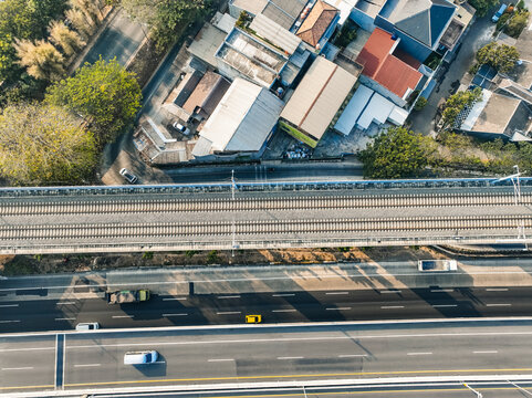 Aerial view of a railway track running parallel to a multi-lane highway with vehicles and residential buildings in Bekasi Barat, West Java, Indonesia.