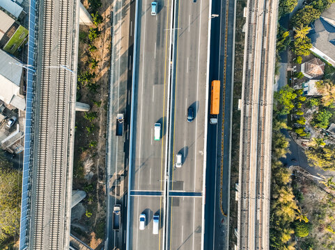Aerial view of a highway with moving cars and trucks, flanked by parallel railway tracks in Bekasi Barat, West Java, Indonesia.