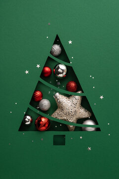 Green paper cutout Christmas tree filled with red and silver ornaments and a glittering star for holiday greeting on vertical bright green blank space