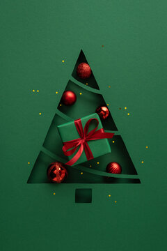 Green paper Christmas tree cutout with red ornament and wrapped gift for Merry Christmas and Happy New Year on vertical green table background