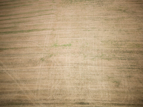 Aerial view of a harvested agricultural field with patches of green vegetation and soil textures in Marpingen, Saarland, Germany.