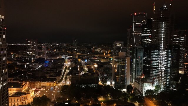 Aerial view of the illuminated skyline at night, featuring towering skyscrapers, glowing city streets, and dense urban architecture in Frankfurt am Main, Hessen, Germany.