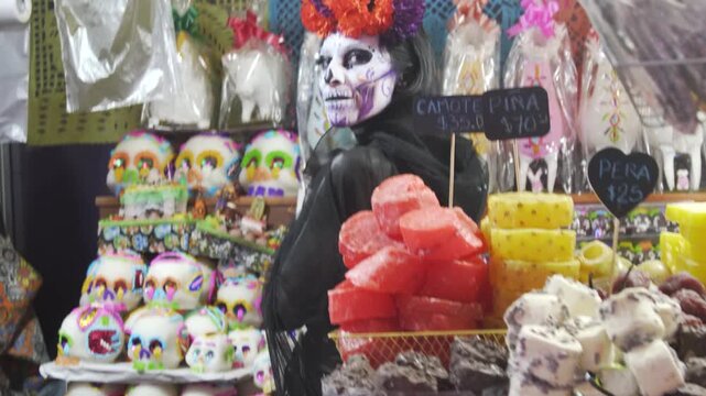 Catrina vendor posing behind traditional Mexican candy stall