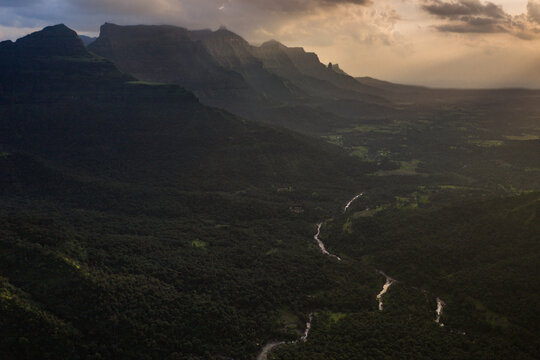 Aerial view of Kalu Water Fall surrounded by lush green mountains and a winding river under dramatic sunset light in Khireshwar, Maharashtra, India.